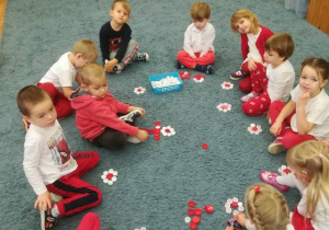 Dzieci na dywanie komponują kwiatki z plastikowych korków białych i czerwonych.